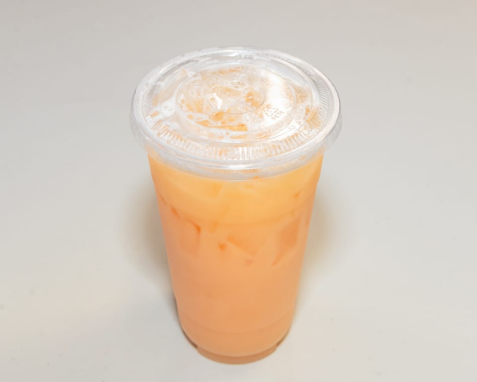A plastic cup of iced Thai tea with a clear lid, filled with ice and a creamy orange beverage.