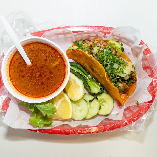 Birria taco with cilantro, onions, and a side of consommé, lemon, cucumber, and jalapeño.