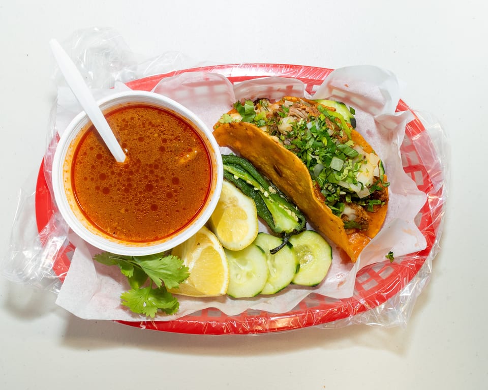 Birria taco with cilantro, onions, and a side of consommé, lemon, cucumber, and jalapeño.