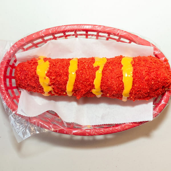 A bright red Flamin' Hot Cheeto corn dog with yellow cheese sauce in a red basket.