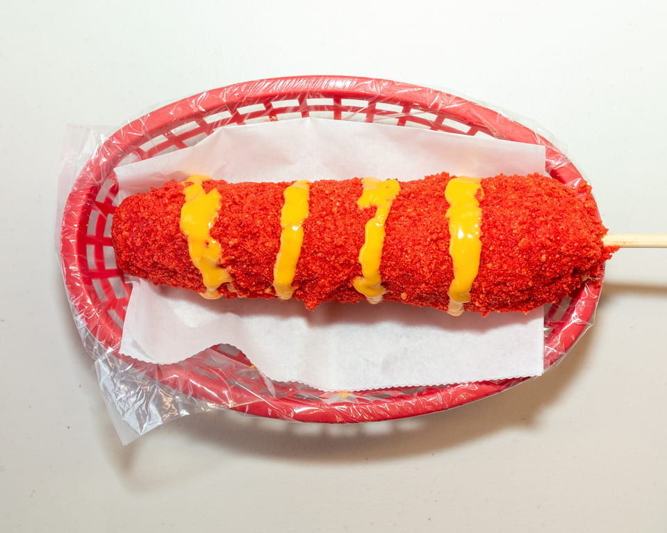 A bright red Flamin' Hot Cheeto corn dog with yellow cheese sauce in a red basket.