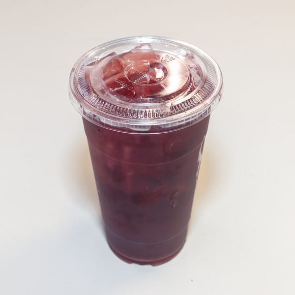 A clear plastic cup filled with a dark red beverage and ice, topped with a clear lid.