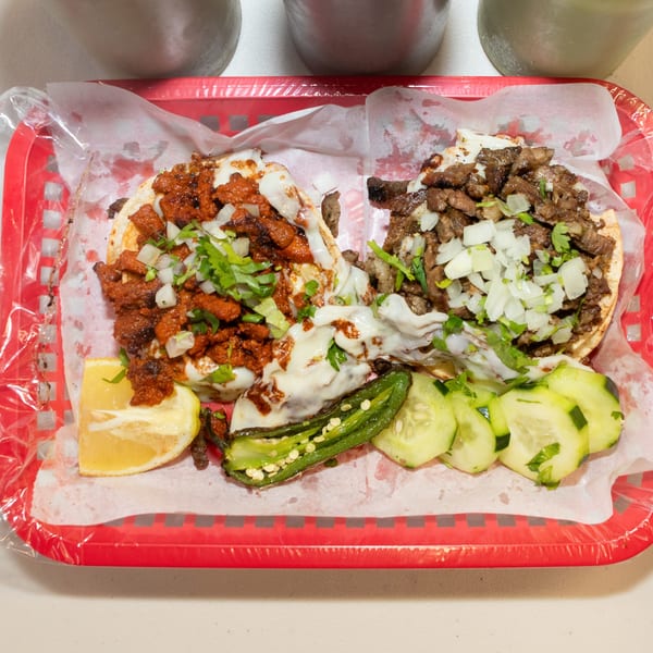 Two tacos, one al pastor and one carne asada, with grilled jalapeño, lemon, and cucumber slices.